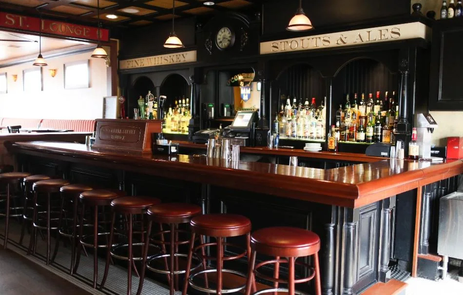 The long first-floor bar at the Dublin House, red-topped stools along the mahogany, whiskey lit under a carved FINE WHISKEY board