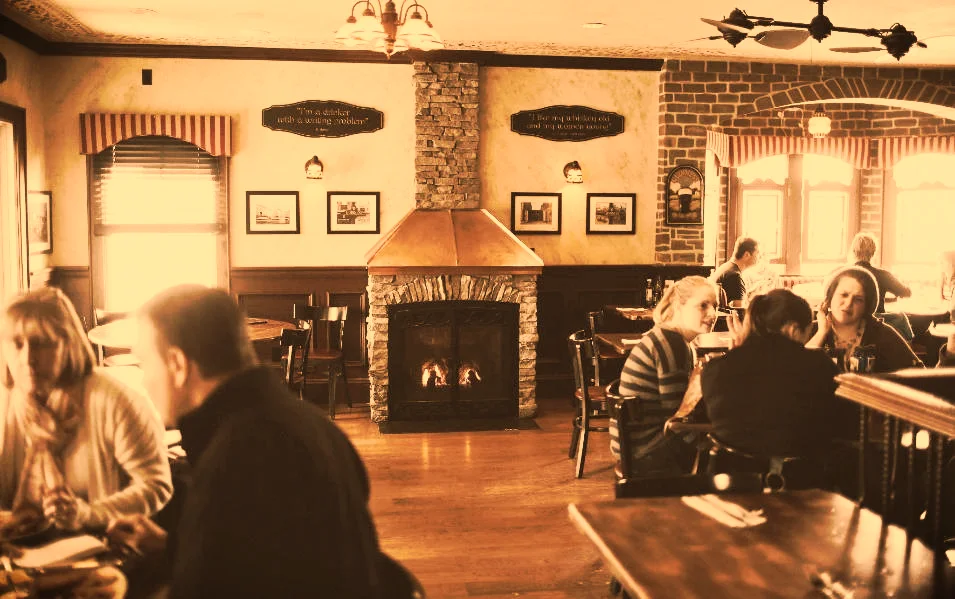 The fireplace room at the Dublin House, a lit hearth in a brick chimney breast, tables filled under arched window valances