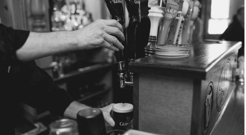 A bartender at the Dublin House drawing a pint of Guinness in two parts, two Guinness fonts above the settled glass